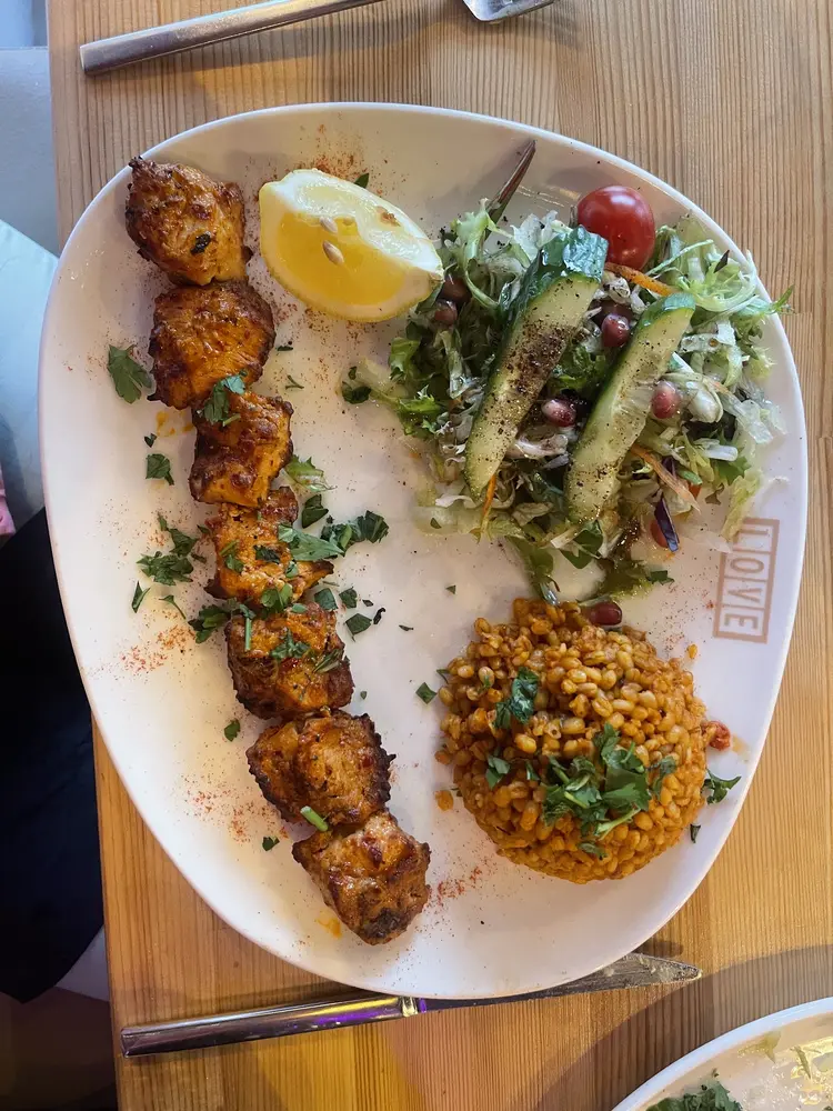 Grilled chicken shish skewer served with bulgur pilaf, salad and lemon on a LOVE branded plate