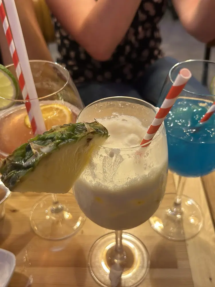 Three cocktails in stemmed glasses with lime, pineapple and striped paper straws on a wooden table