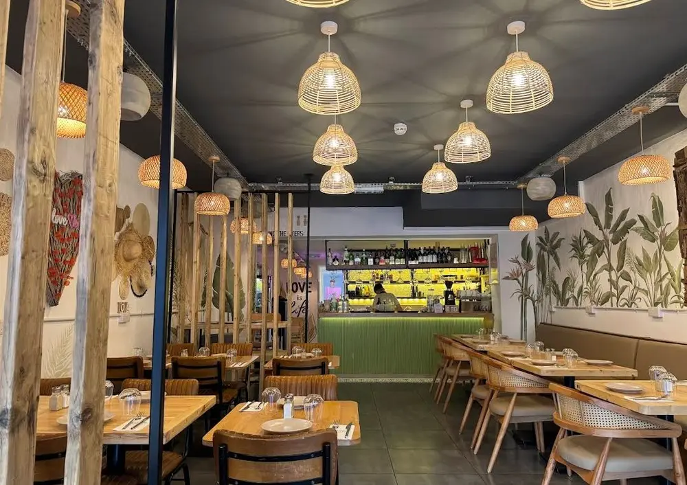 Inside Love Dulwich, woven rattan pendant lights above wooden tables with the green bar counter at the back